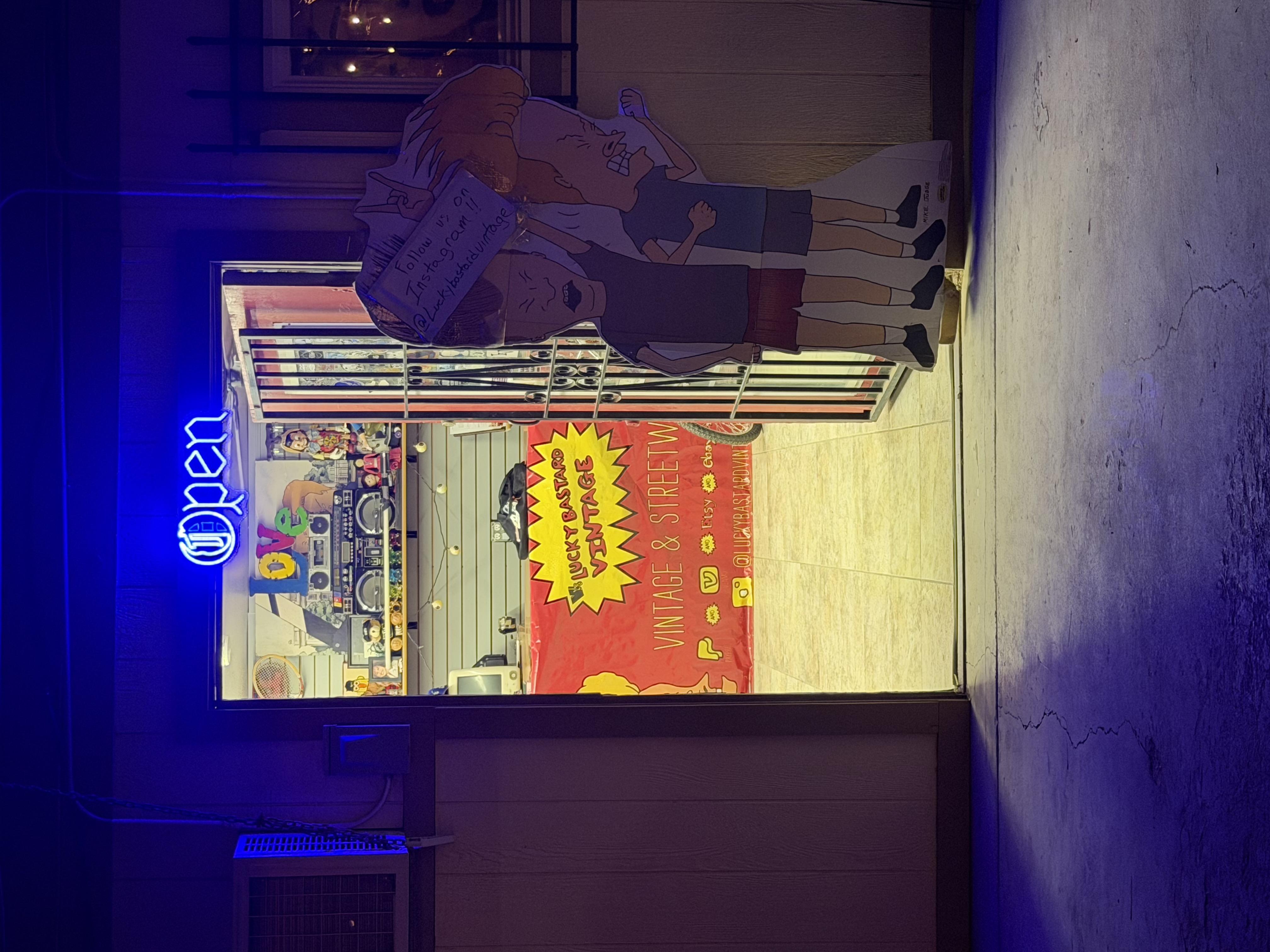 Lucky Bastard Vintage storefront entrance with neon Open sign at night